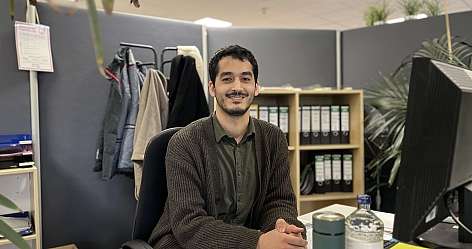 junger Mann sitzt am Schreibtisch und lächelt