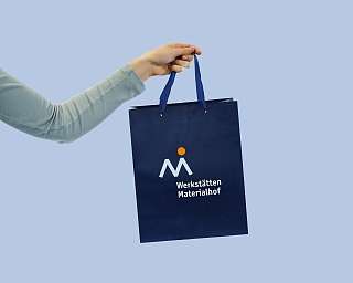 Eine Hand hält eine dunkelblaue Einkaufstasche mit Logo.